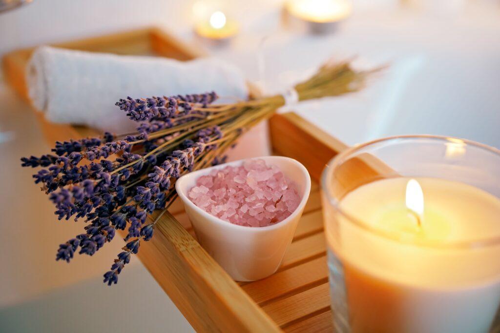 Eine Kerze, Lavendel und Duftsteine liegen auf einer Badewanne 