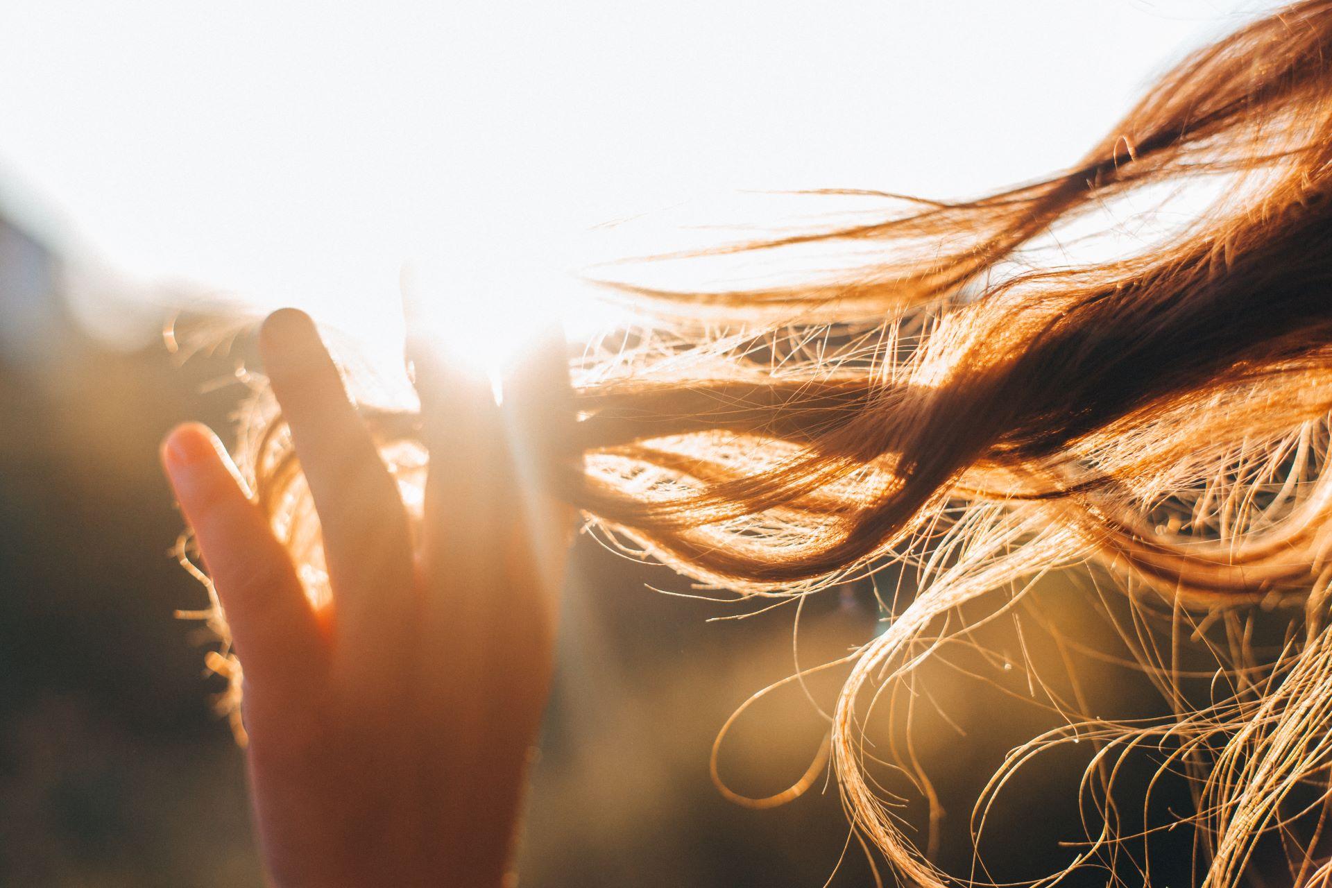 Die Frau berührt eine Haarlocke. DIe Sonne scheint. Selektiver Fokus