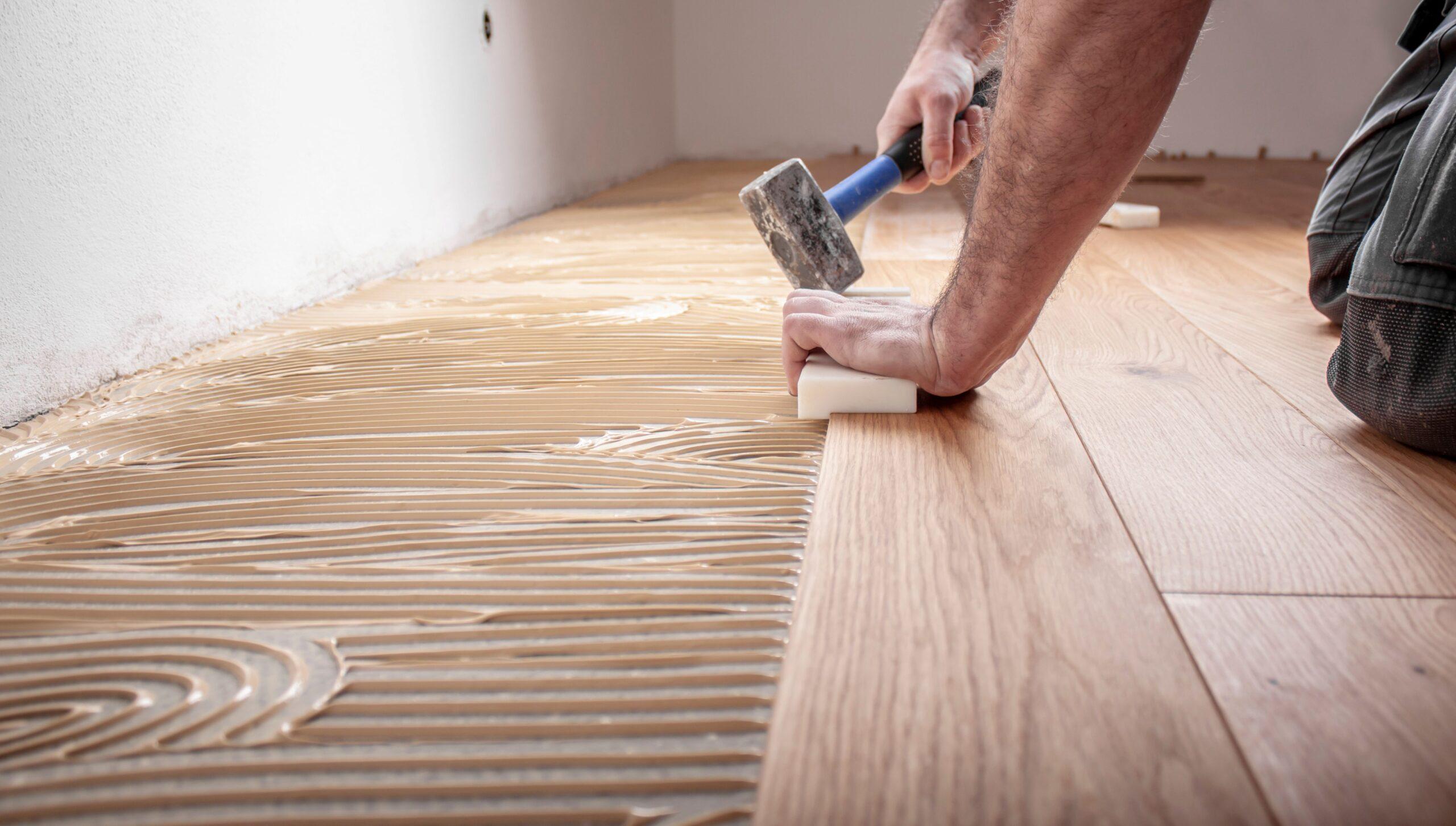 Wohnungssanierung Berlin: Fachgerechte Bodenverlegung mit Holzkleber und Hammer bei laufender Renovierung