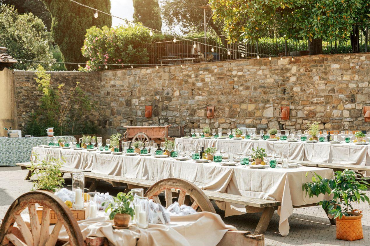 gedeckte festtafeln im hof mit kraeutern und holzelementen bei einer hochzeit auf dem bauernhof